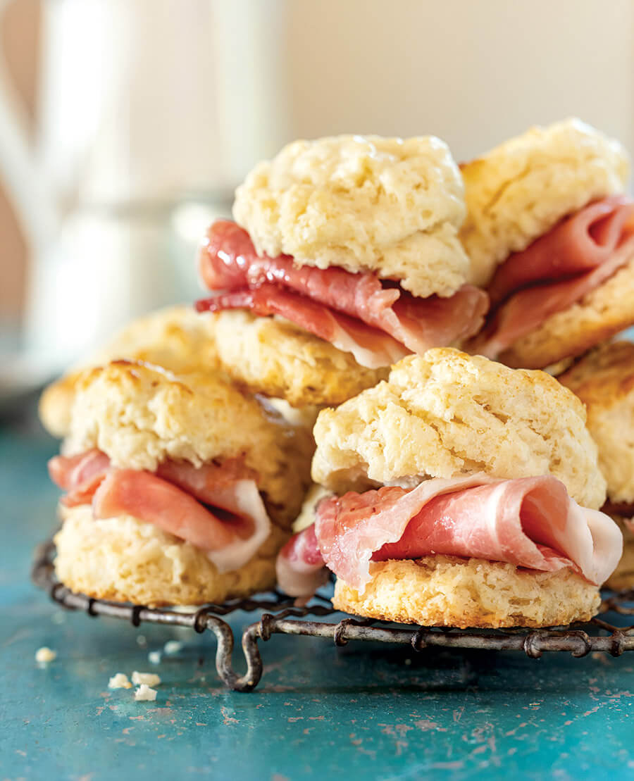 Biscuits stacked with slices of ham on a wire rack.
