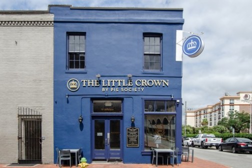 Blue storefront labeled 'The Little Crown by Pie Society' with outdoor seating, sign above door.