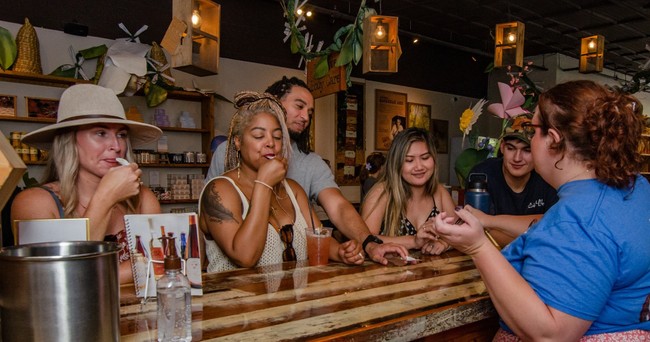 Group of people tasting products at a wooden counter in a cozy store.