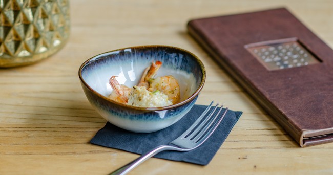 Bowl of shrimp and rice on a napkin with a fork, beside a closed notebook on a wooden table.