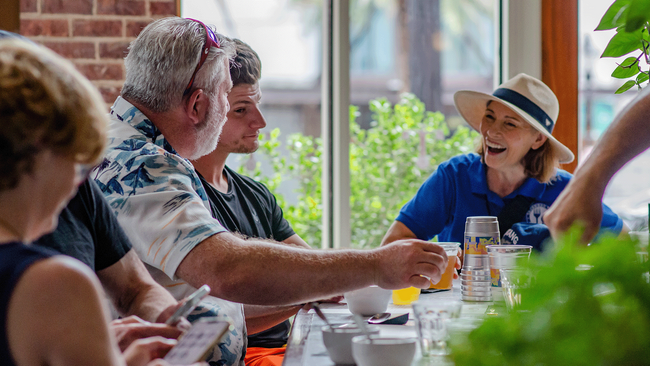 Group of people sitting at a table, talking and smiling in a brightly lit room.