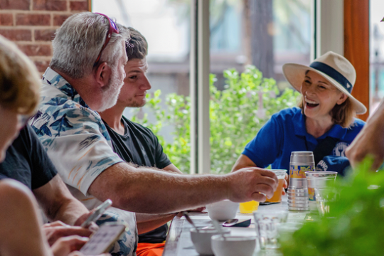Group of people sitting at a table, talking and smiling in a brightly lit room.