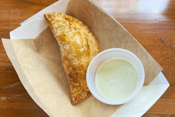 Pastry in tray with small cup of creamy dipping sauce on wooden table.