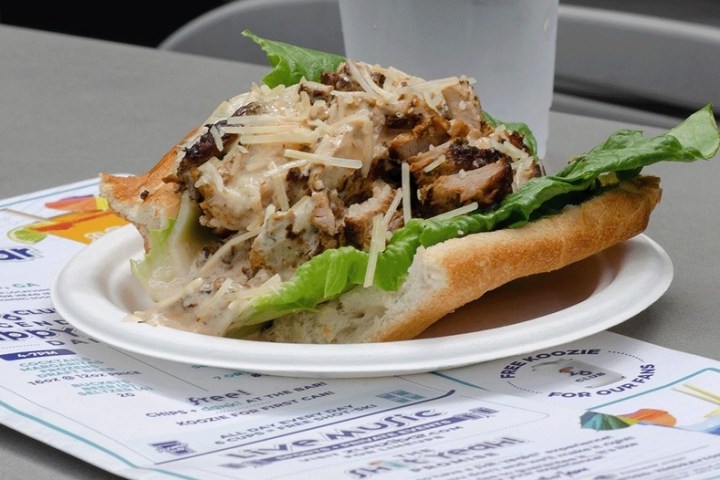 Chicken Caesar sandwich on a paper plate with lettuce and parmesan cheese.