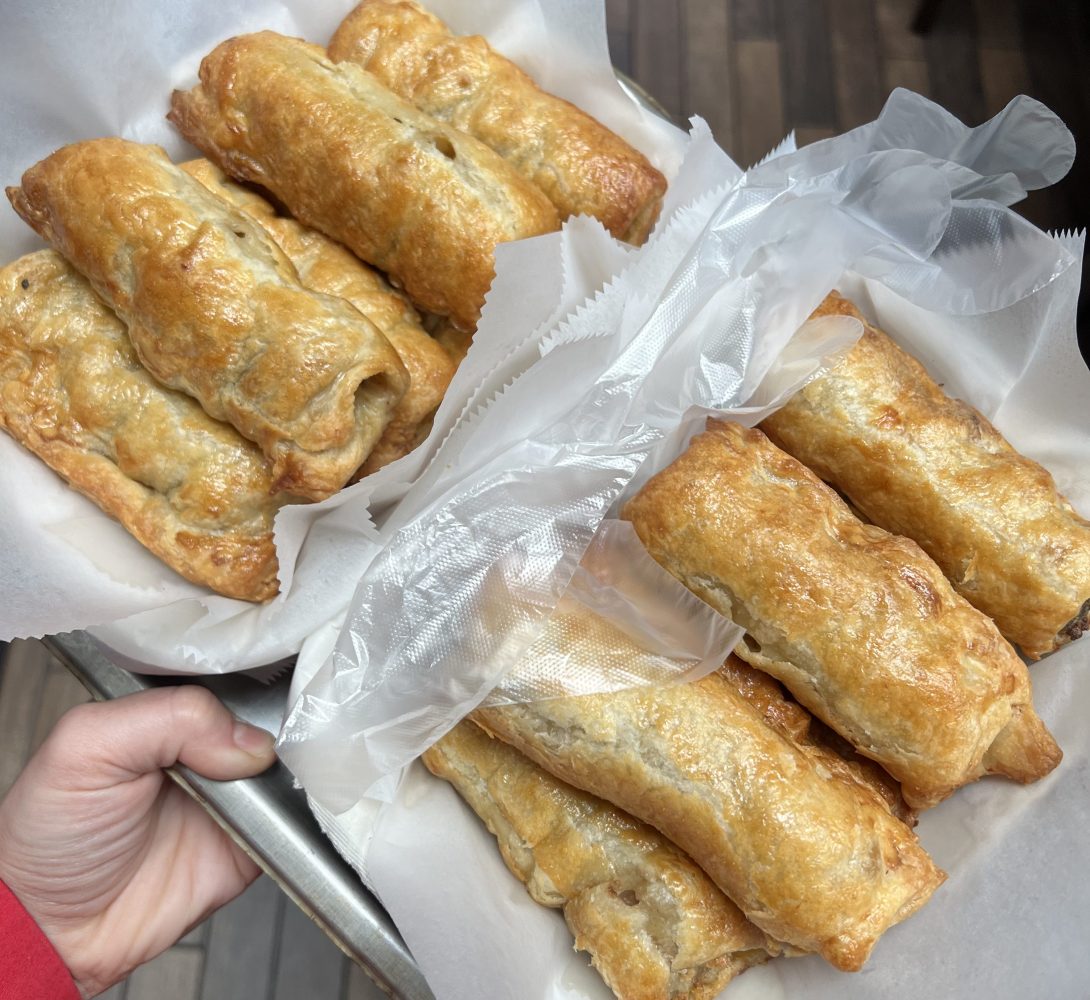 Person holding trays with golden-brown pastries on parchment paper.