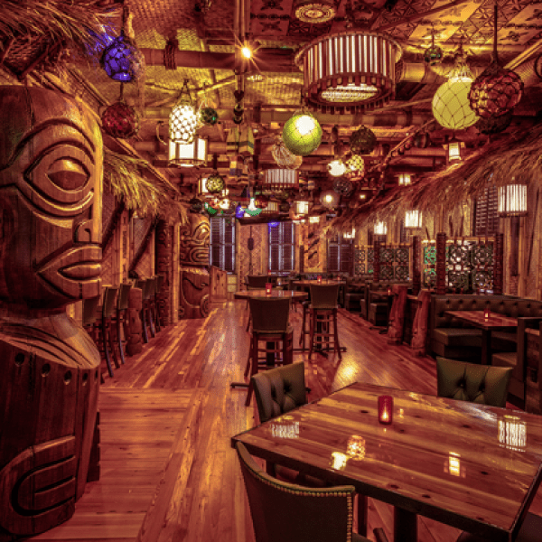 Cozy tiki-themed restaurant with wooden carvings and colorful hanging lights.