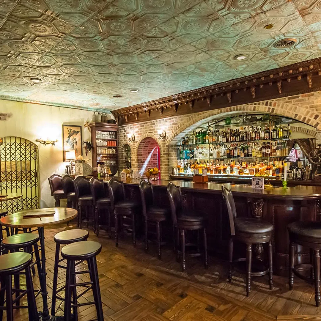 Cozy bar with vintage decor, wooden stools, and a mirrored back bar filled with bottles.