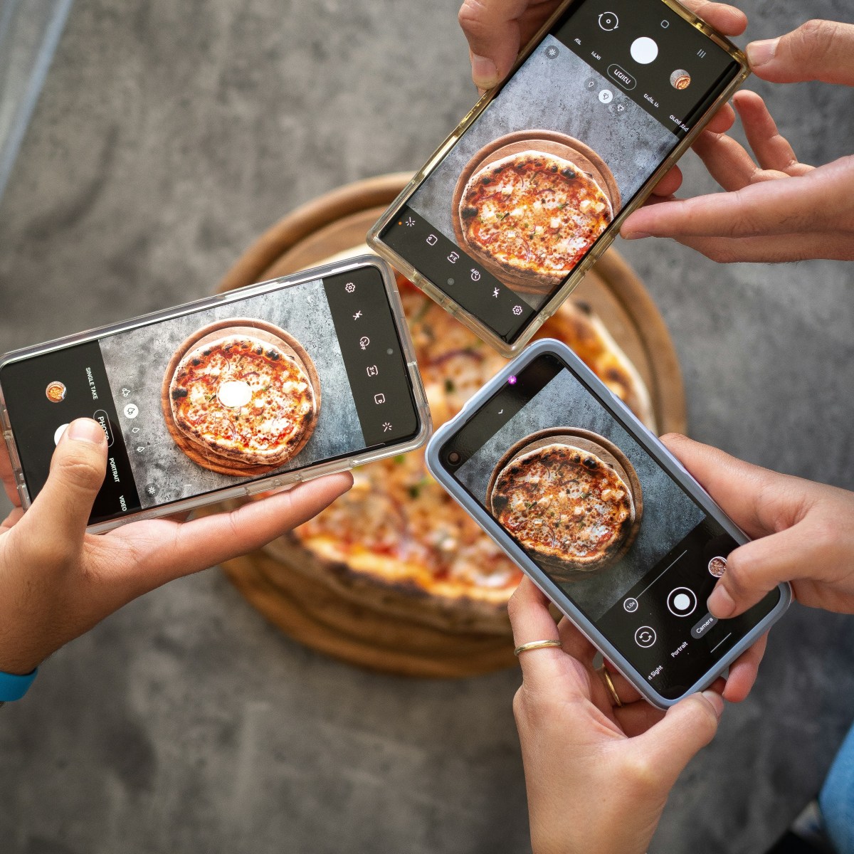 Four people taking photos of a pizza with smartphones from above.