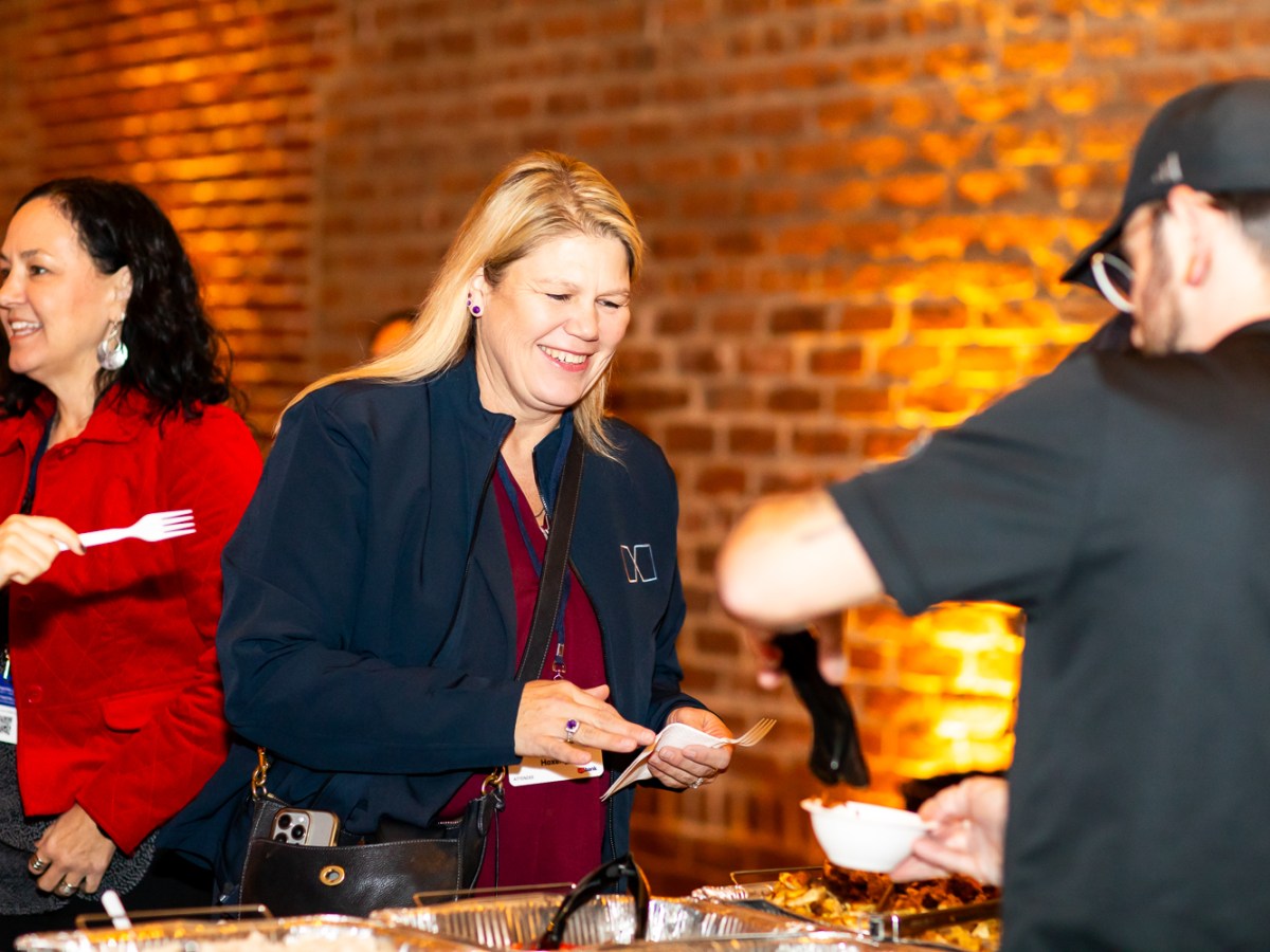 People at a buffet table, smiling, with a brick wall in the background.
