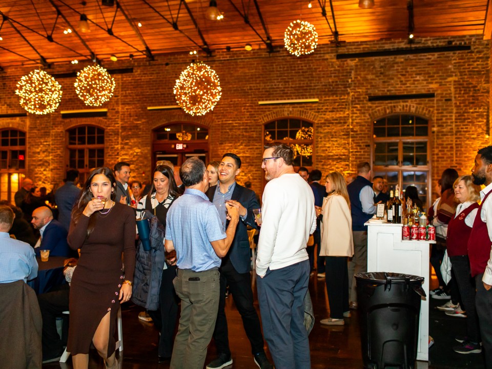 People socializing at an indoor event with drinks, brick walls, and warm lighting.