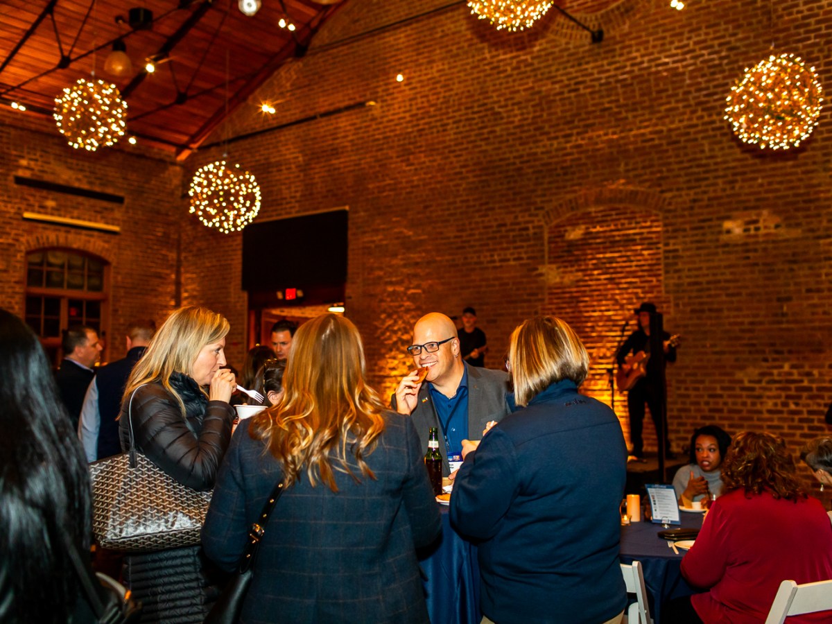 People socializing in a warmly lit brick venue with hanging lights and live music.