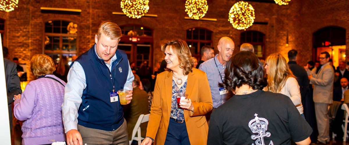 People socializing at an indoor event with food and decorative lights hanging from the ceiling.
