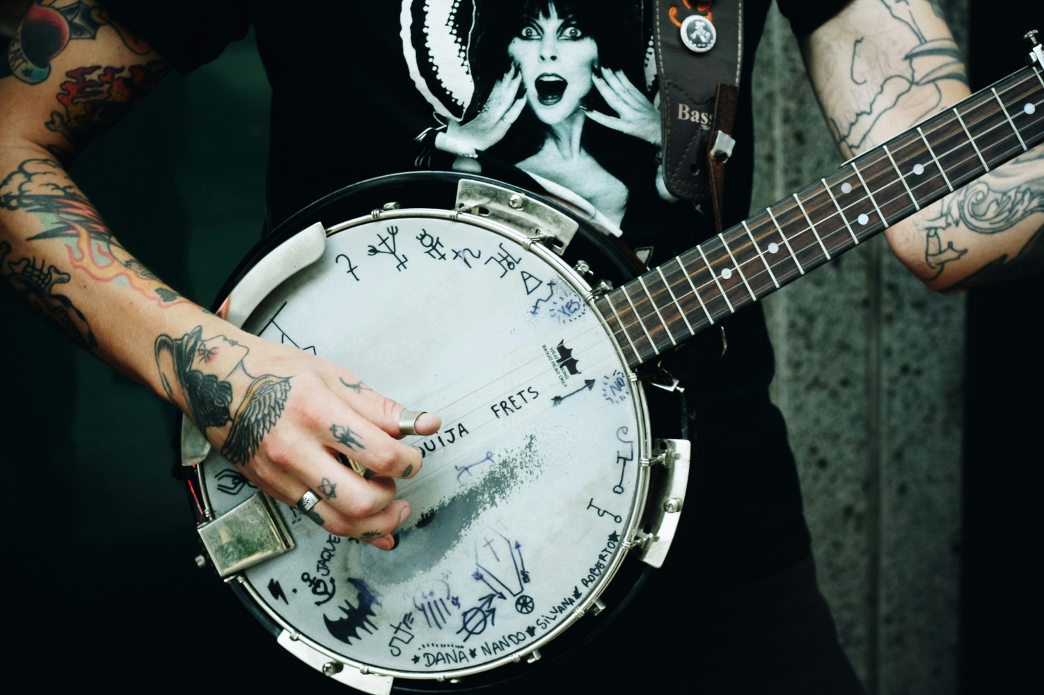 Person with tattoos plays a decorated banjo featuring symbols and writing.