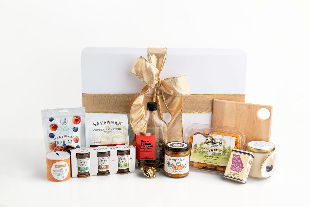 Gift box with gold ribbon, includes snacks, tea, honey, coffee, jam, cheese straws, a board, and candle.