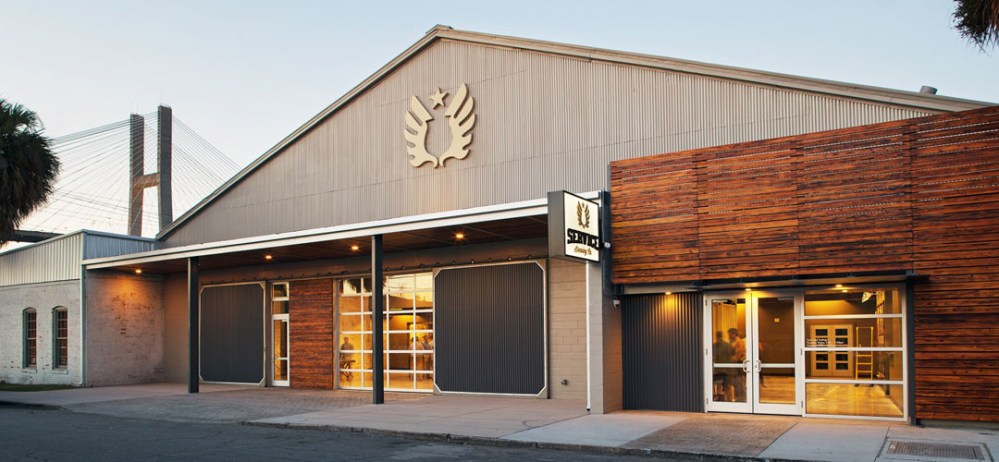 Modern building exterior with industrial design and bridge in background.