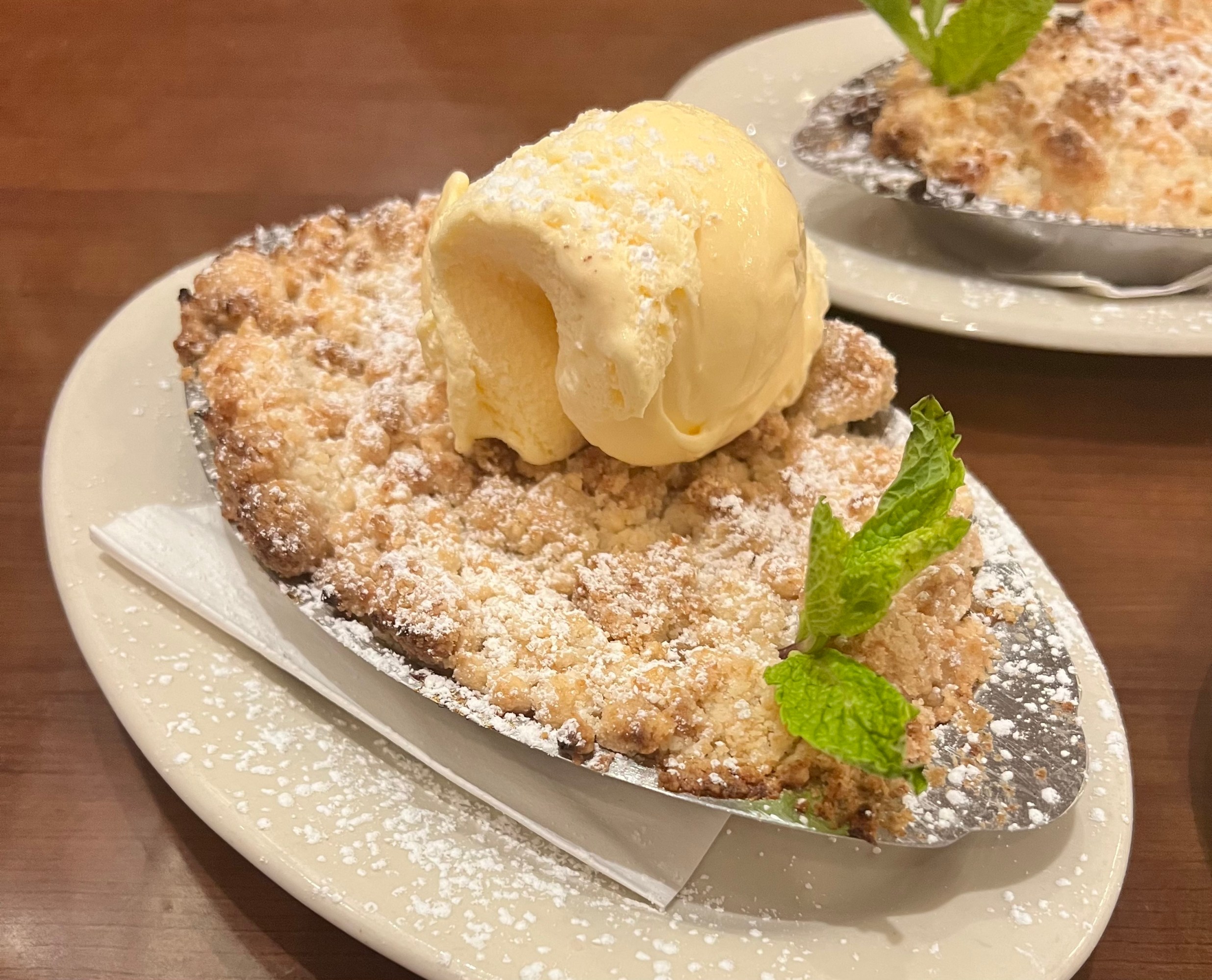 Crumbly dessert topped with vanilla ice cream and mint on a white plate.