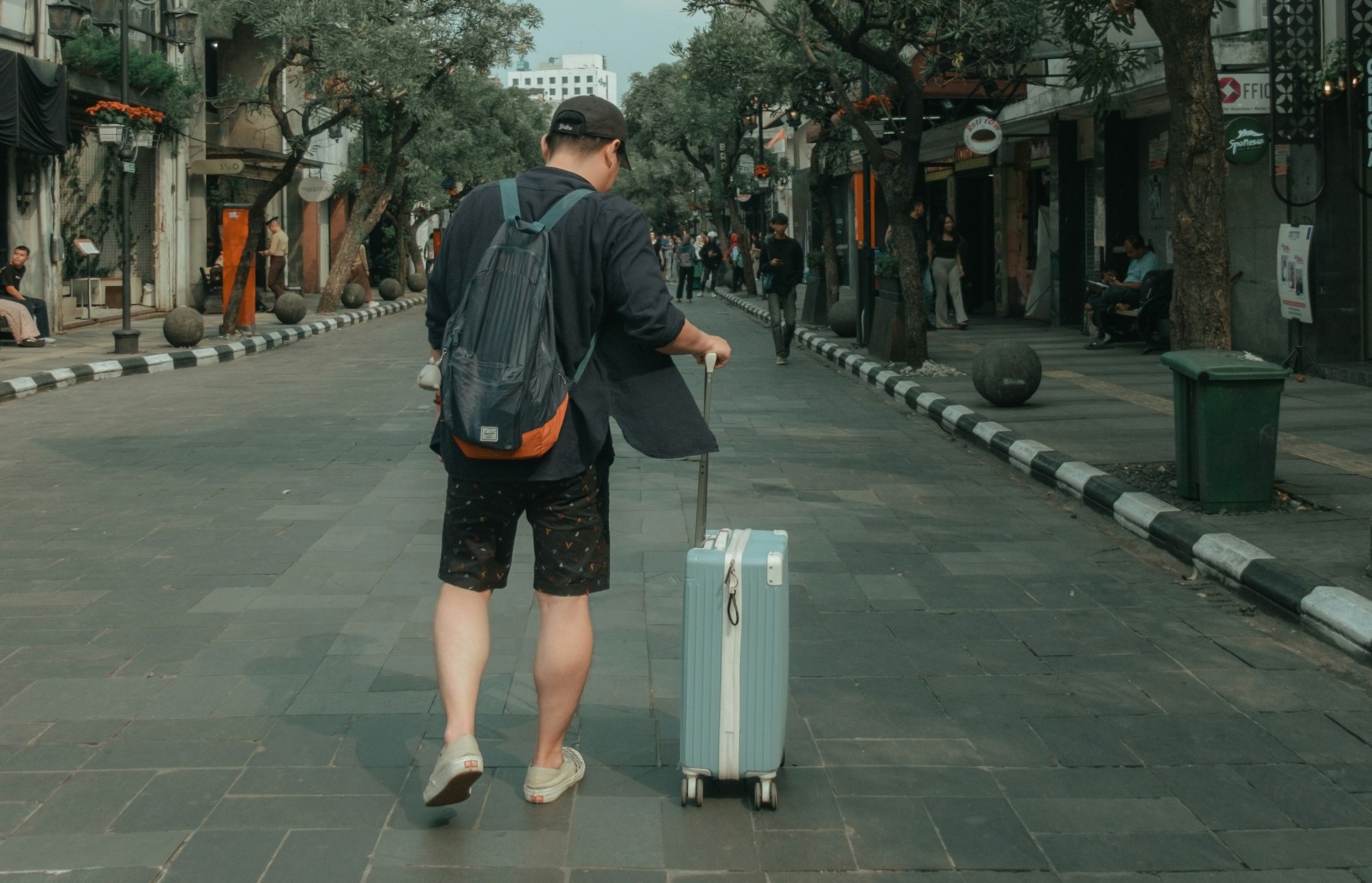 Person with a backpack pulling a suitcase on a city street.