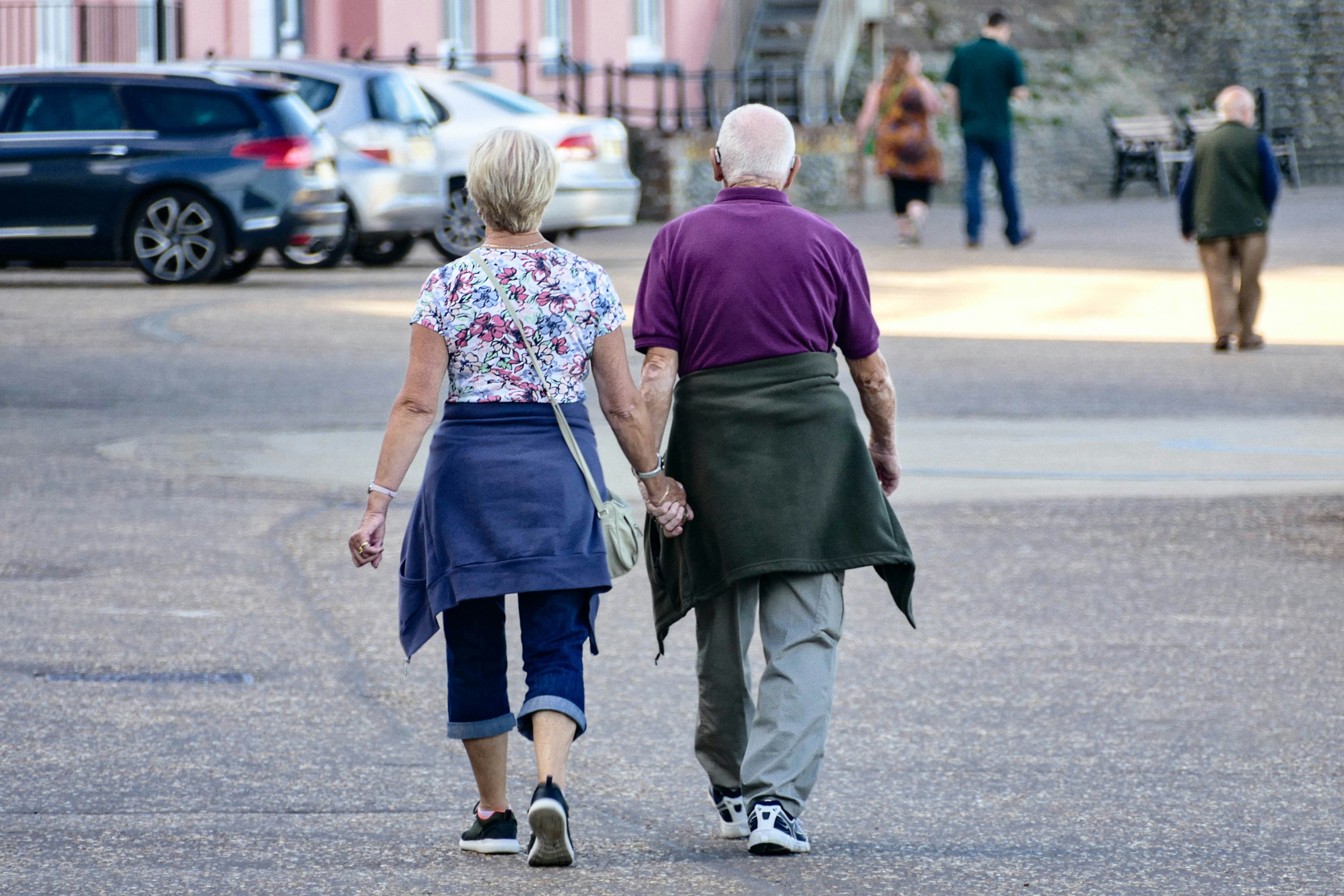 Older couple holding hands, walking on a street.