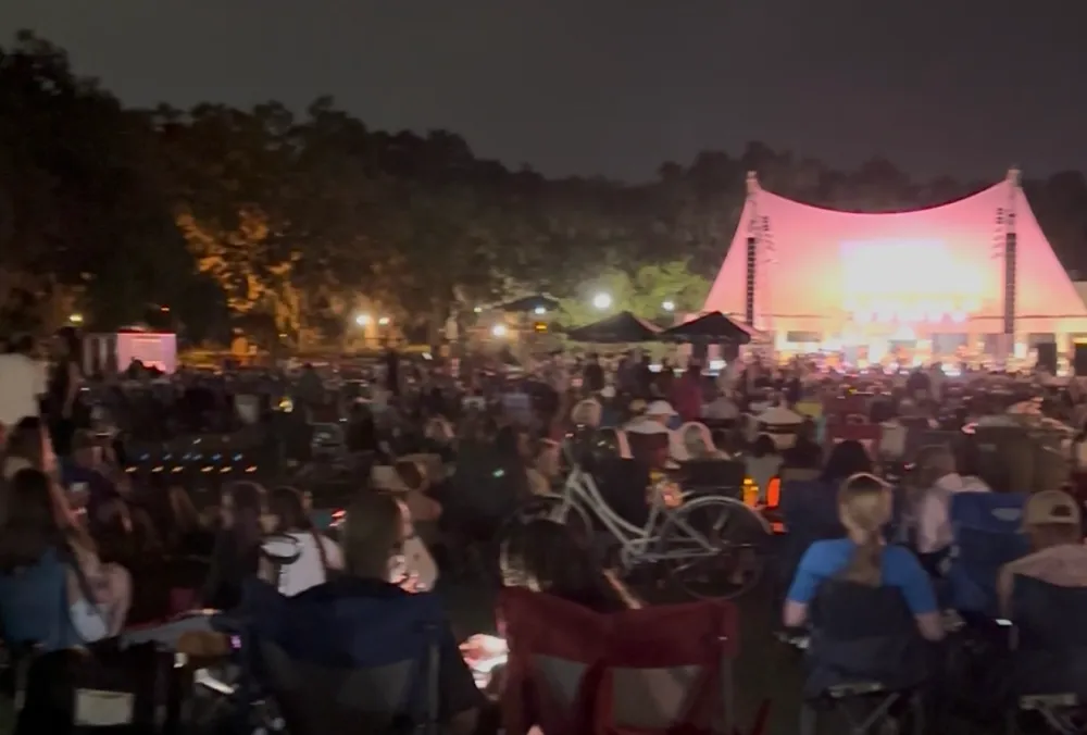 Crowd seated outdoors at night, watching a performance on a lit stage.