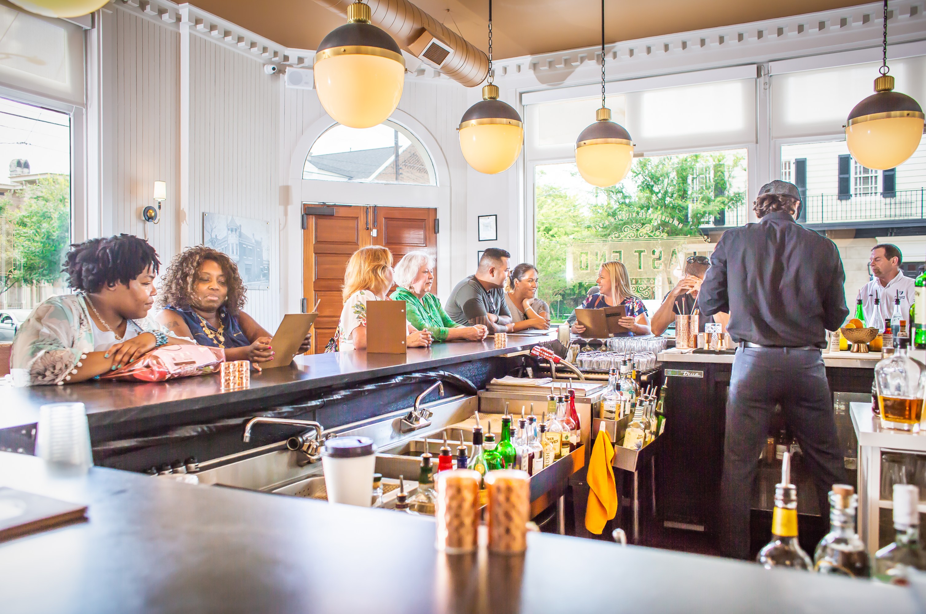 People sitting at a busy bar, bartender serving drinks, daytime.