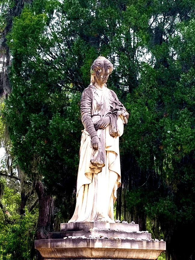 Stone statue of a woman holding scales in a garden setting.